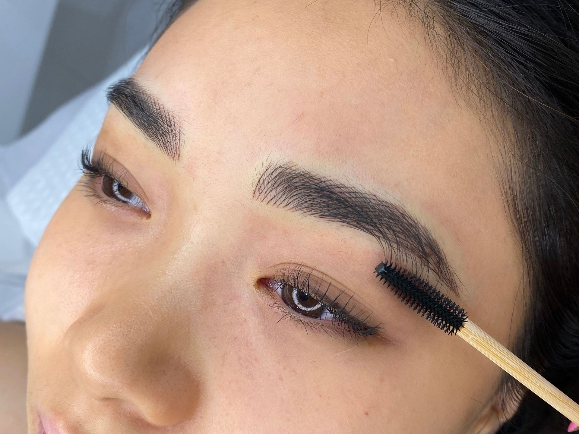 A woman is brushing her eyebrows with a brush — Sibina Cosmetic Tattoo Art In Broadbeach, QLD