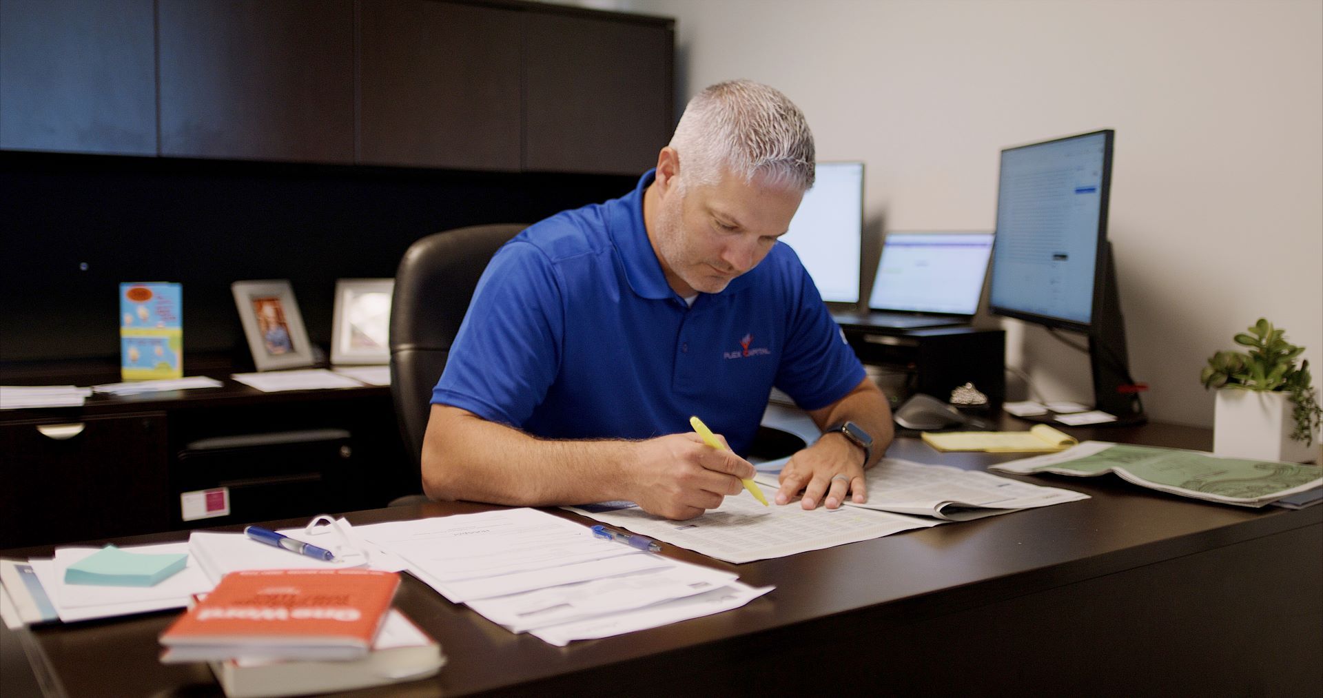 A man in a blue shirt is sitting at a desk writing on a piece of paper.