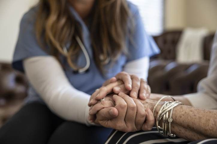 A nurse is holding the hand of an elderly woman.