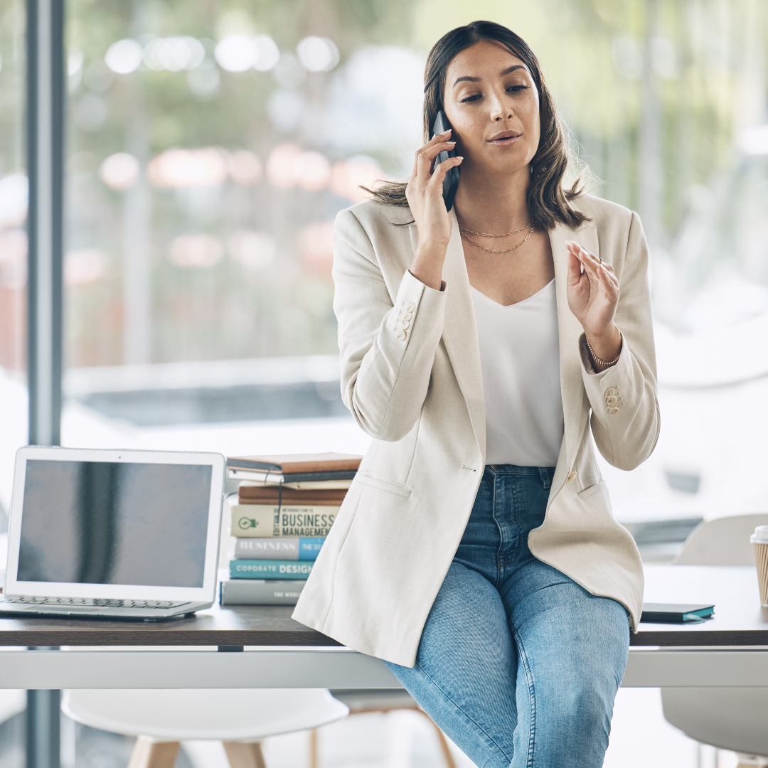 A woman is sitting at a desk talking on a cell phone.