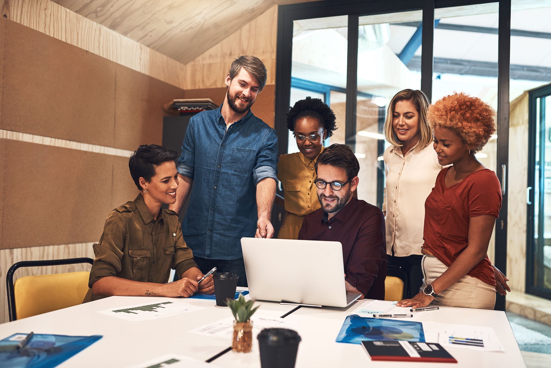 A group of people are standing around a table looking at a laptop computer.