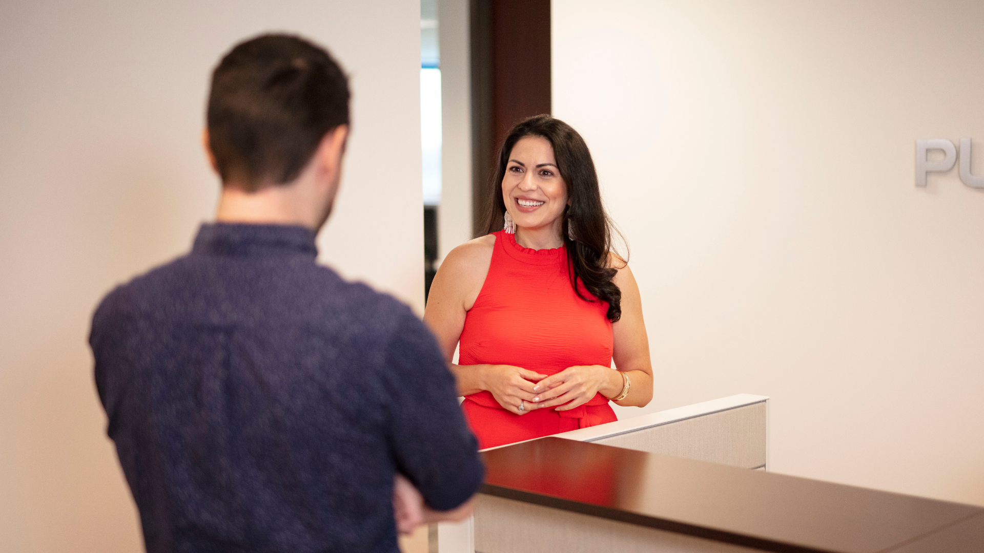 Two women are standing in an office cubicle talking to each other.