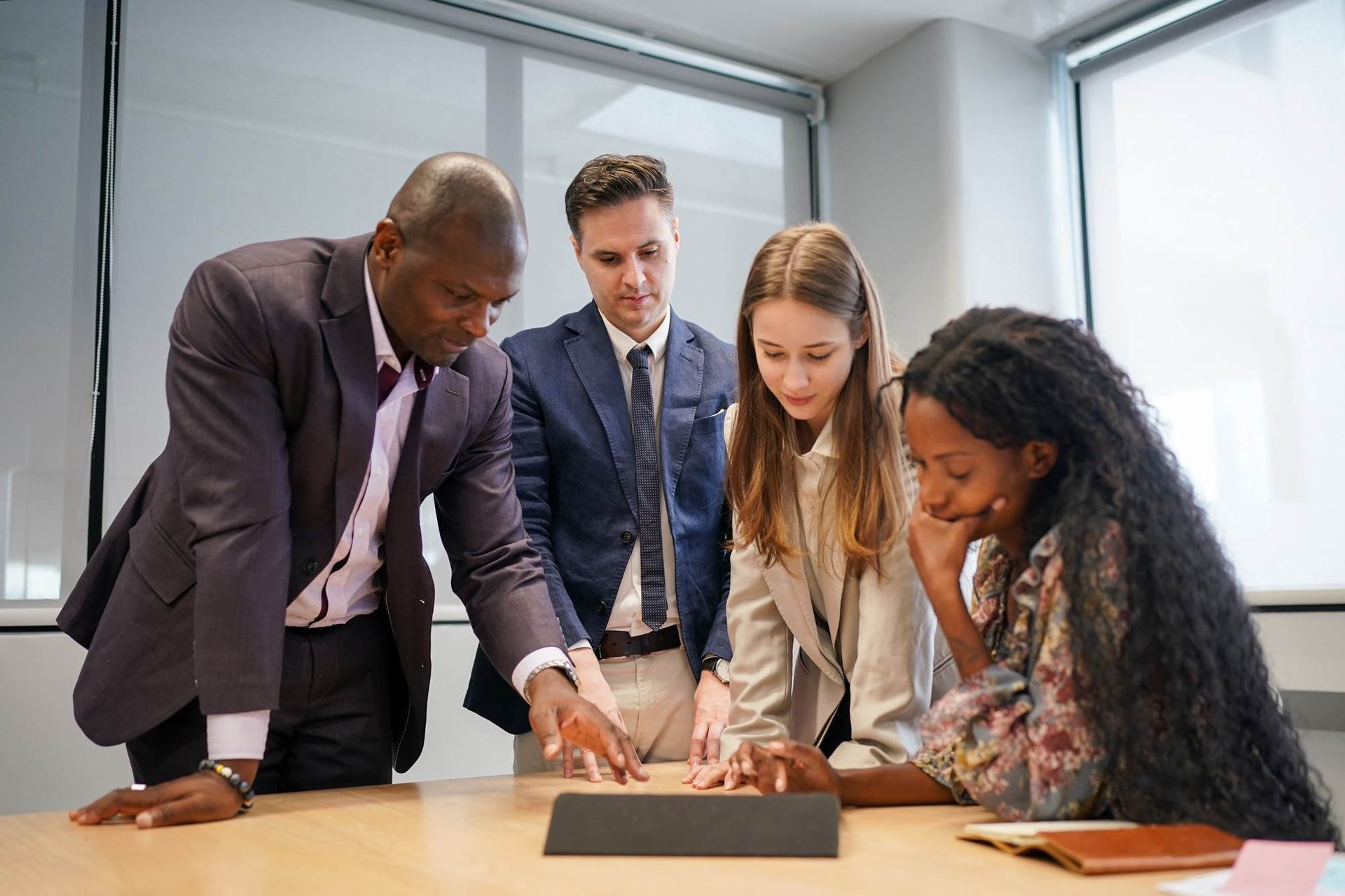 A group of people are standing around a table looking at a tablet.