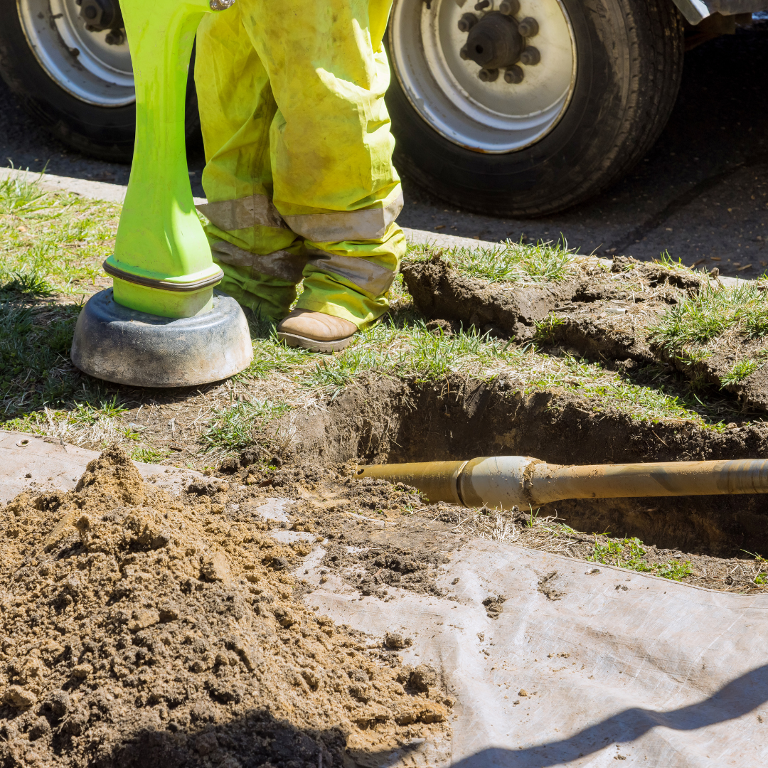 A man in yellow overalls is standing next to a hole in the ground.