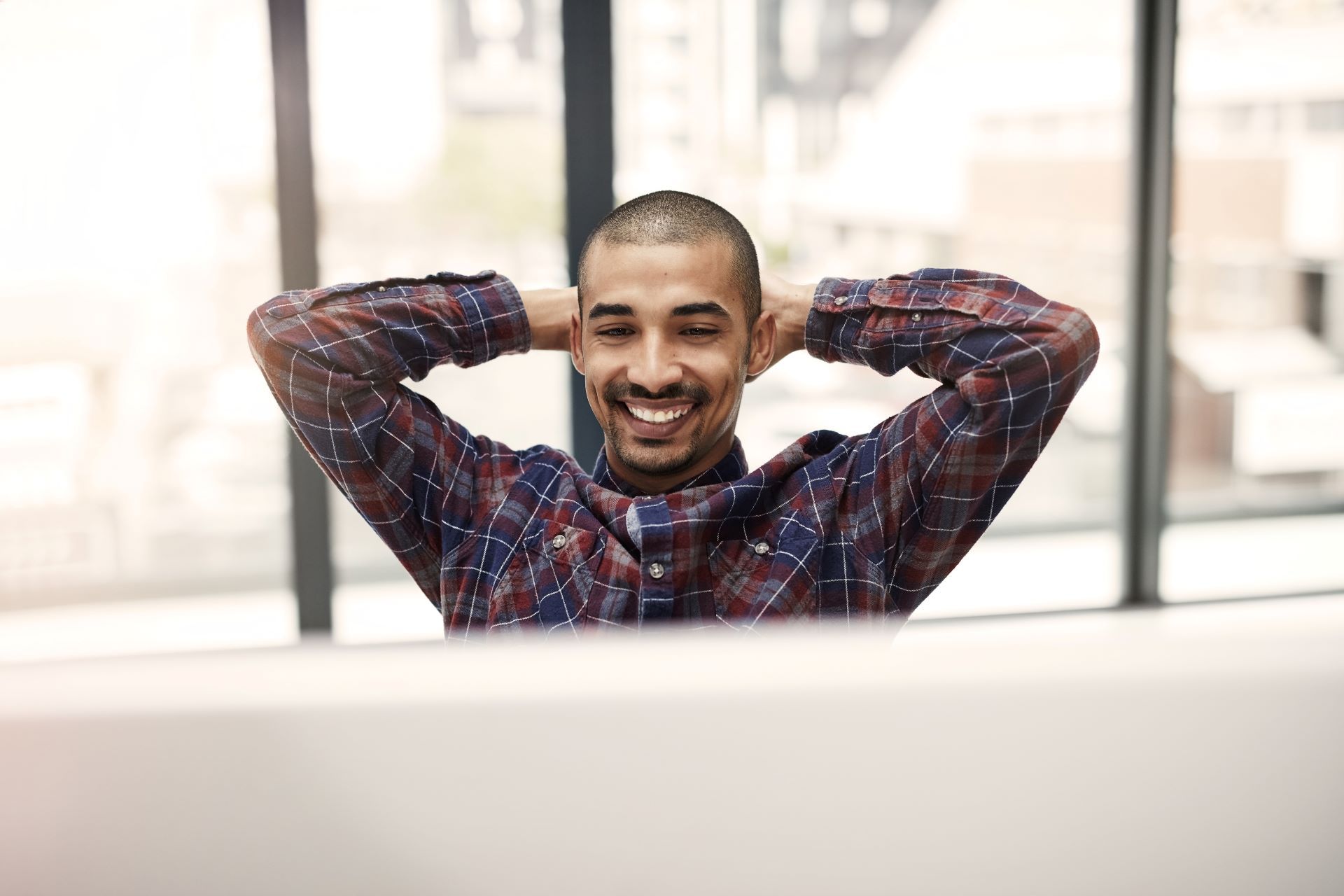 A man is sitting at a desk with his hands behind his head.