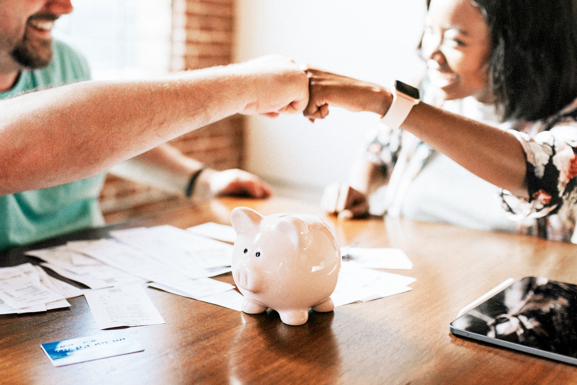 A man and a woman are shaking hands over a piggy bank on a table.