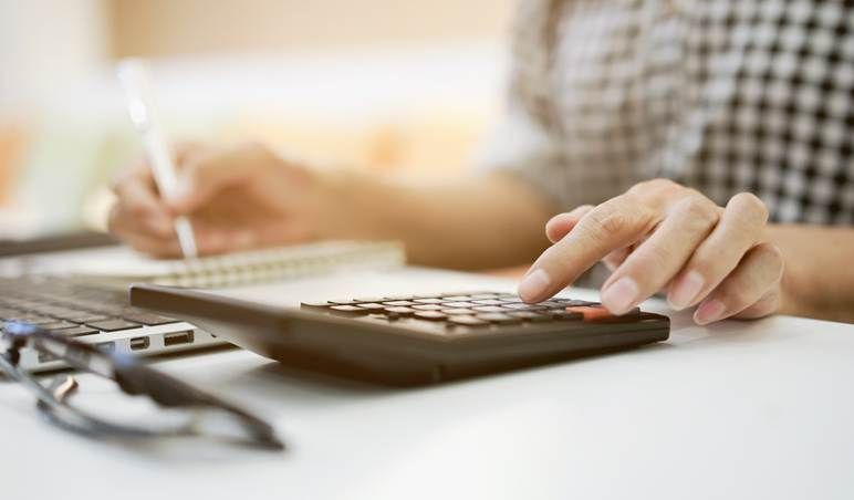 A person is using a calculator while writing in a notebook.