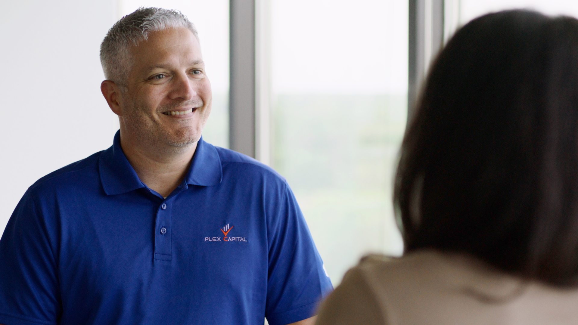 A man in a blue shirt is talking to a woman in front of a window.