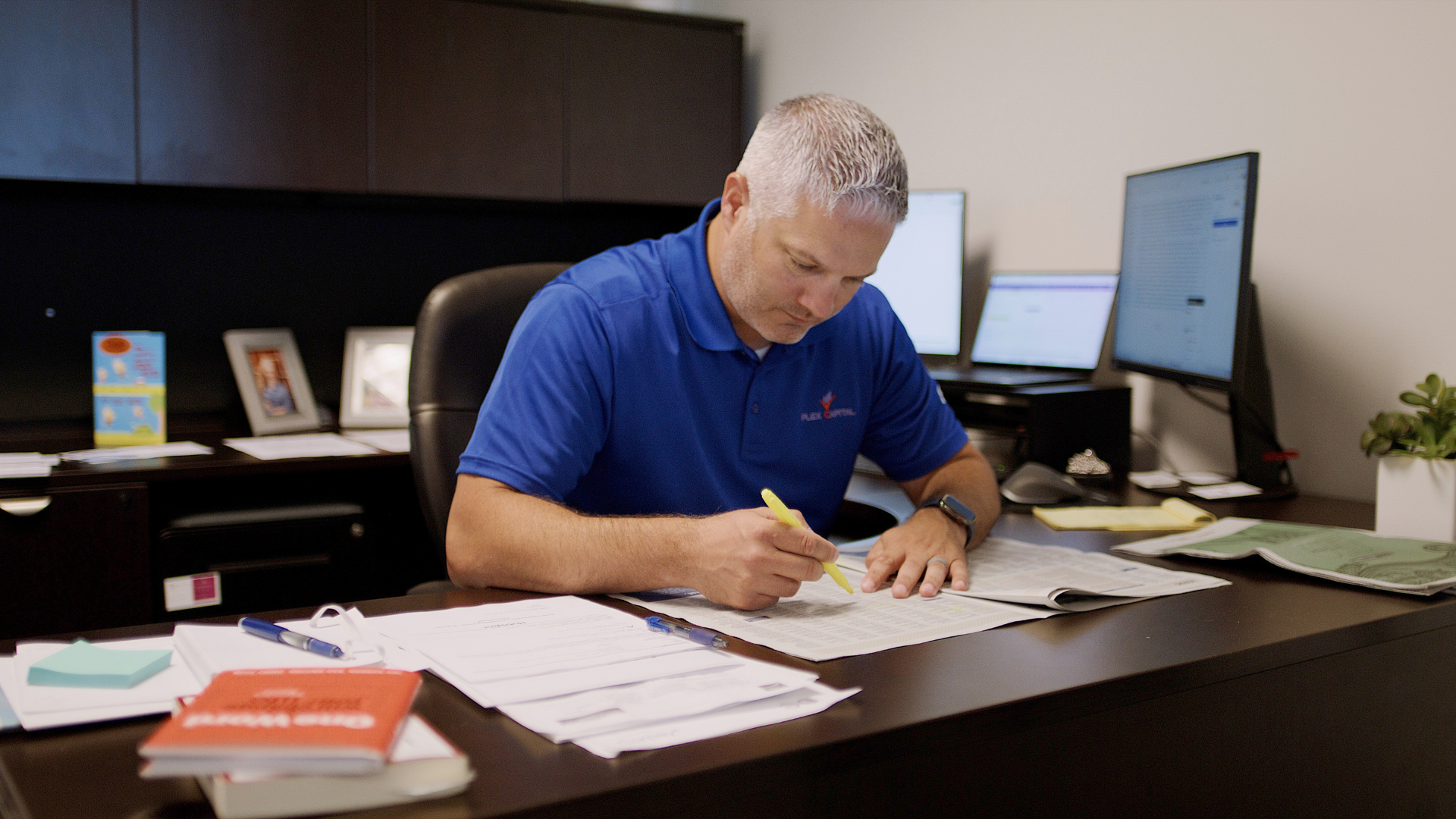 A man is sitting at a desk in an office writing on a piece of paper.