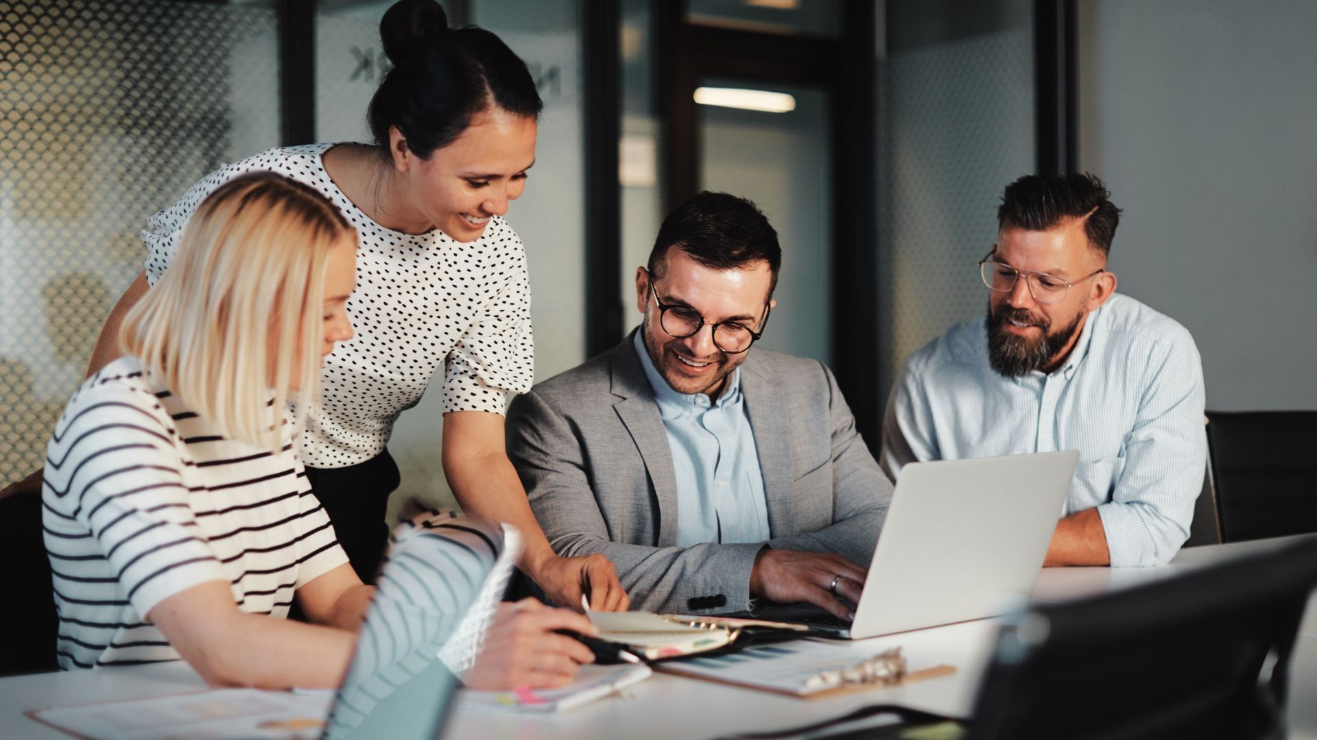 Four people collaborating around a laptop in an office. Smiling and focused, they are discussing.