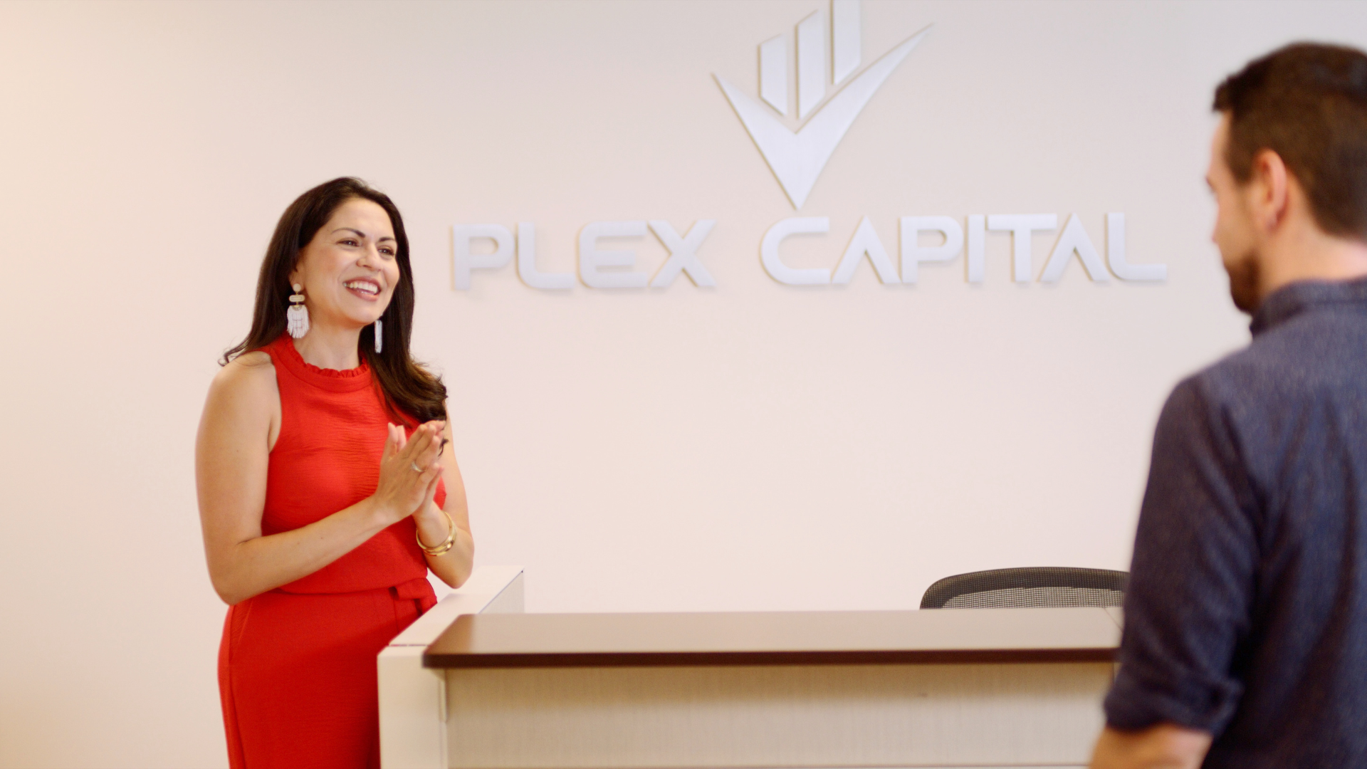 A woman in a red dress is standing next to a man in front of a plex capital sign.