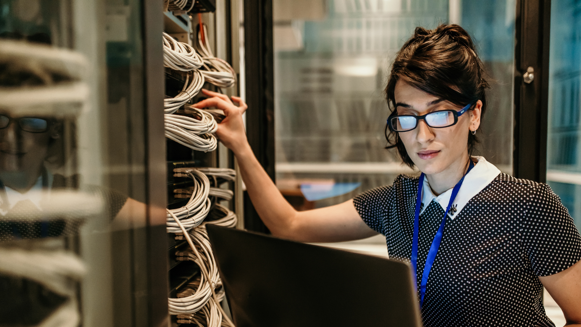 A woman is working on a laptop in a server room.
