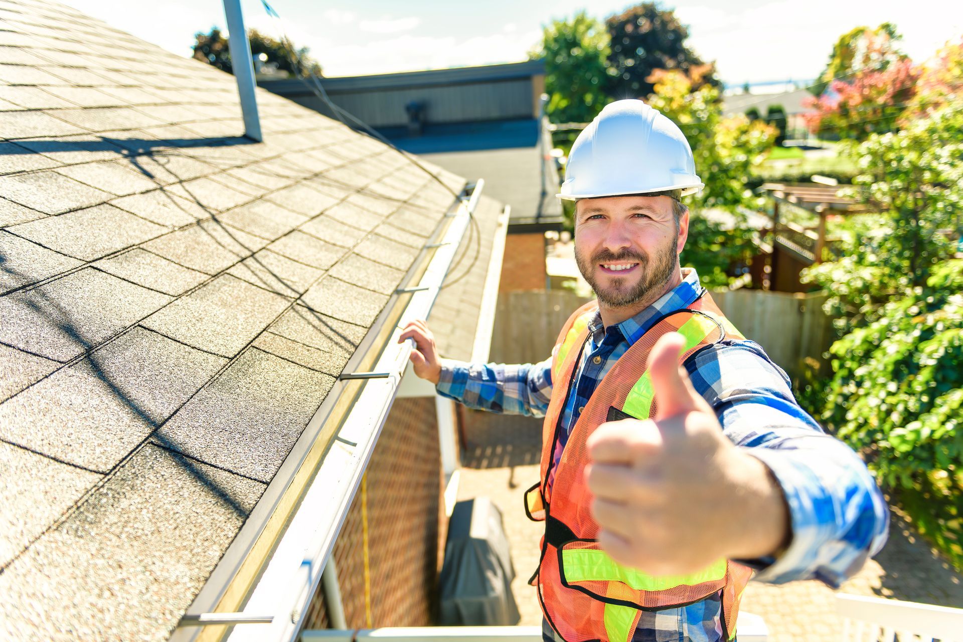 A man is giving a thumbs up while standing on top of a roof.