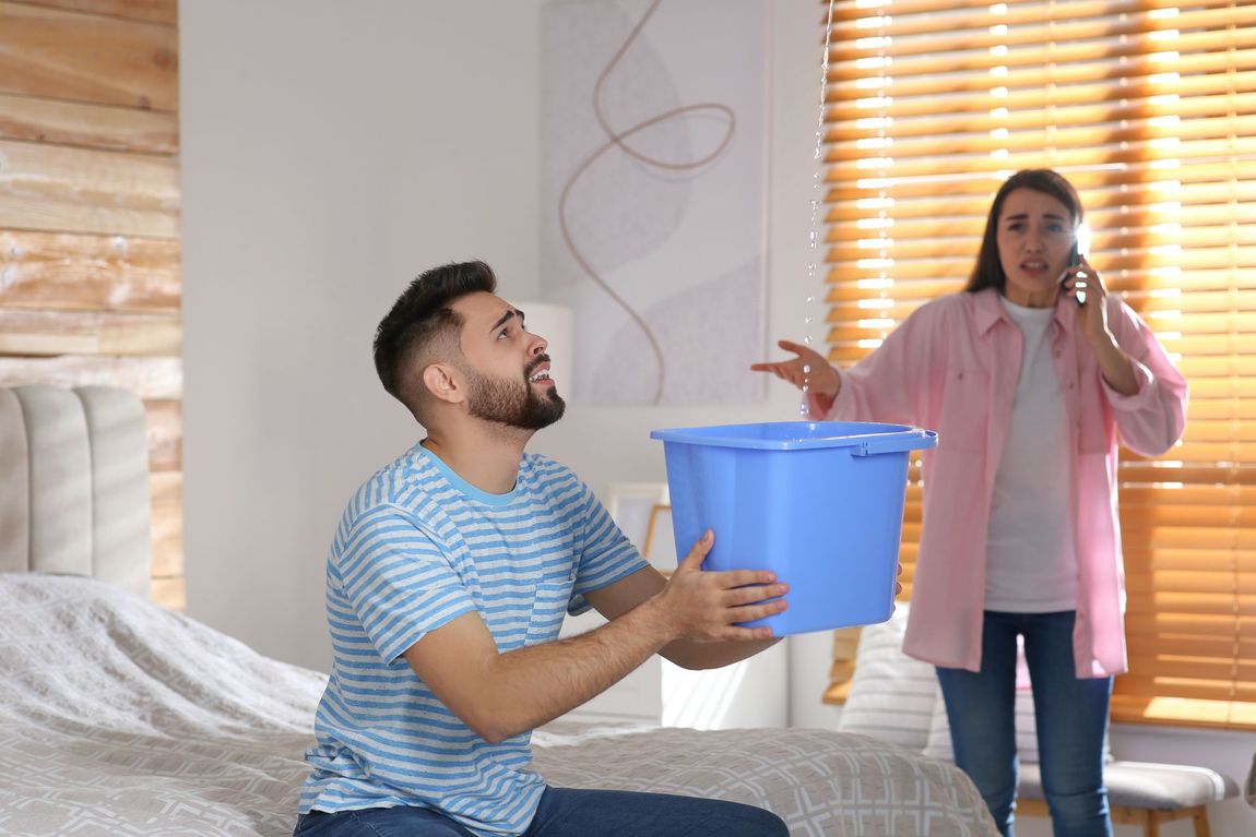 A man is holding a blue bucket while a woman talks on a cell phone.