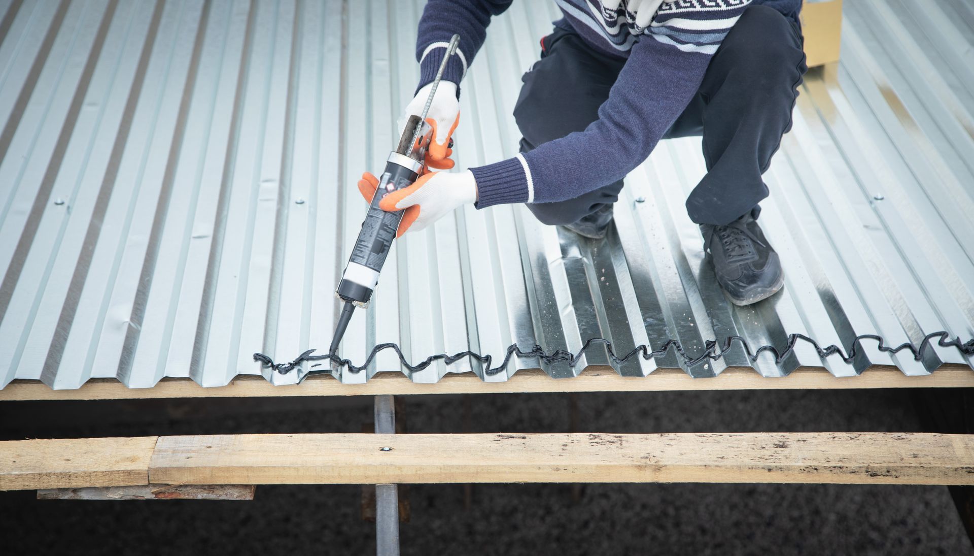 A man is applying sealant to a metal roof.