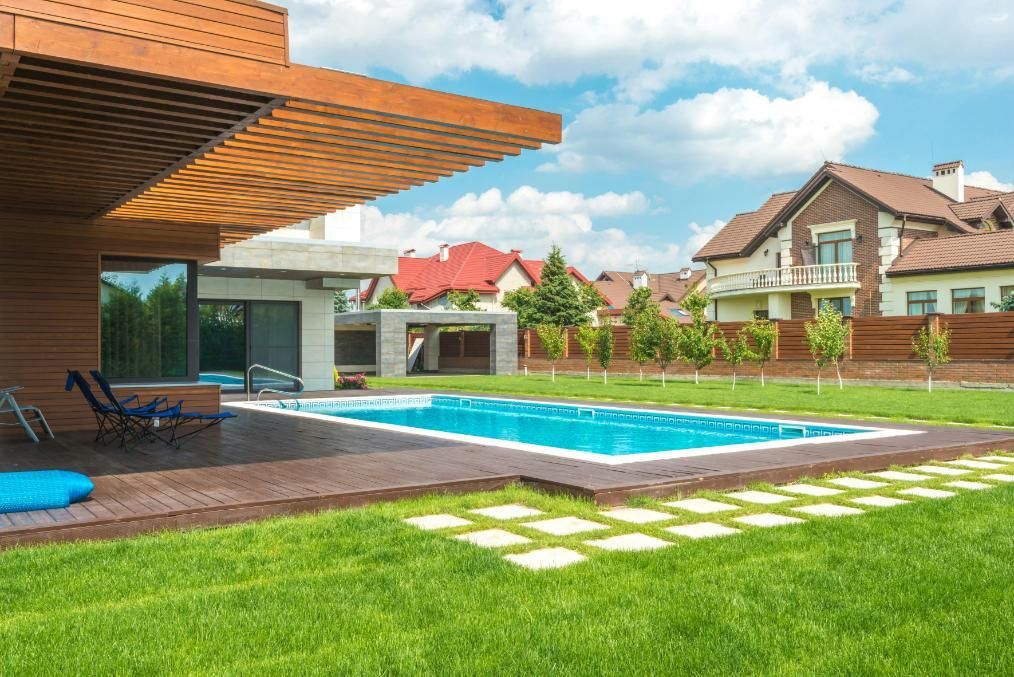 Modern house with pool and wooden deck; green lawn and blue sky.