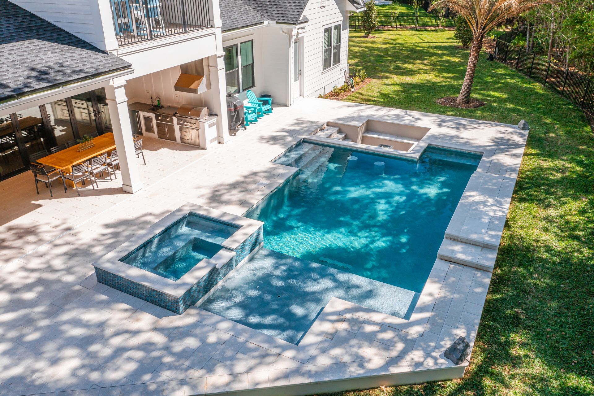 Aerial view of a backyard with a pool and spa next to a white house.
