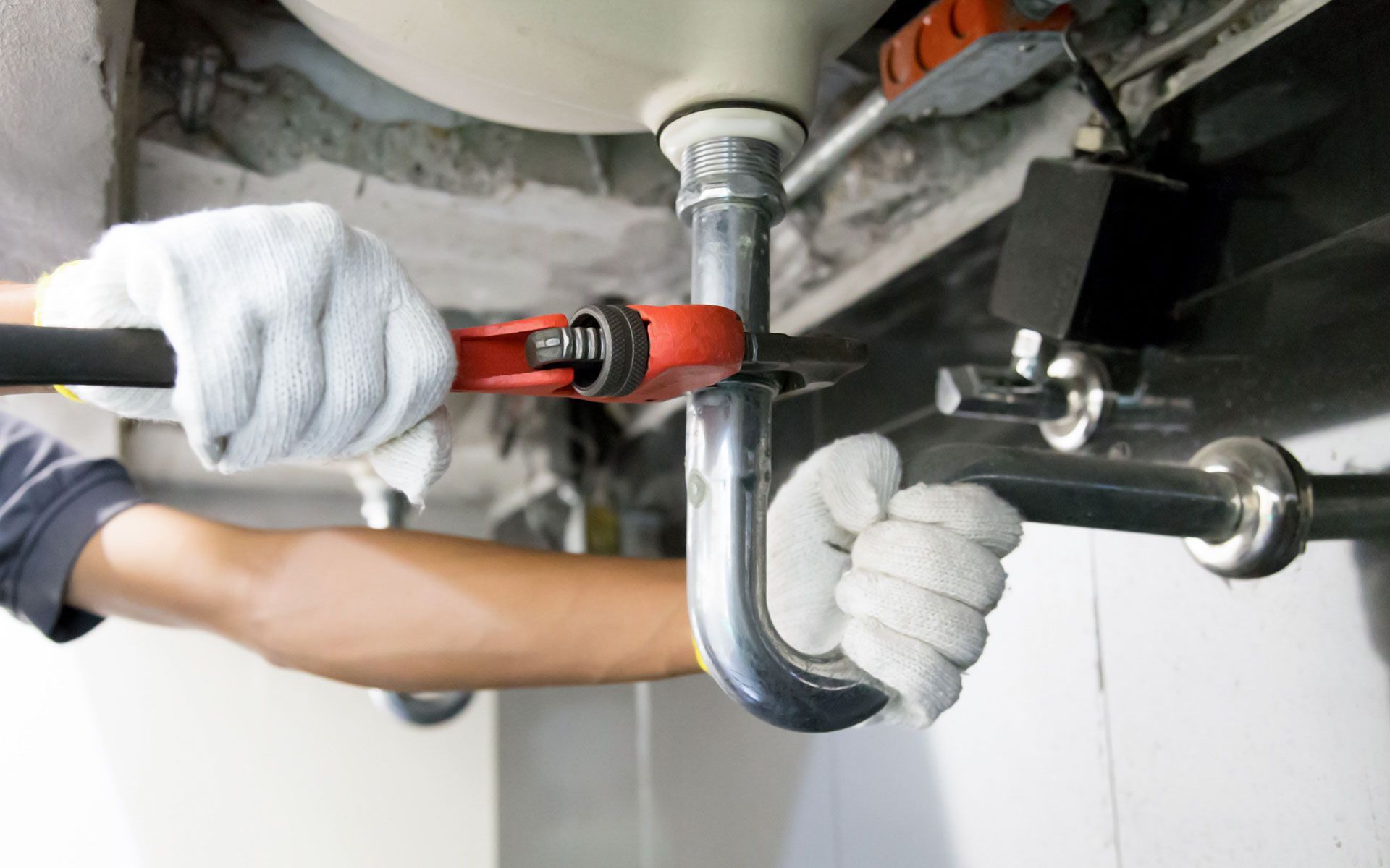 A plumber is fixing a sink pipe with a wrench.