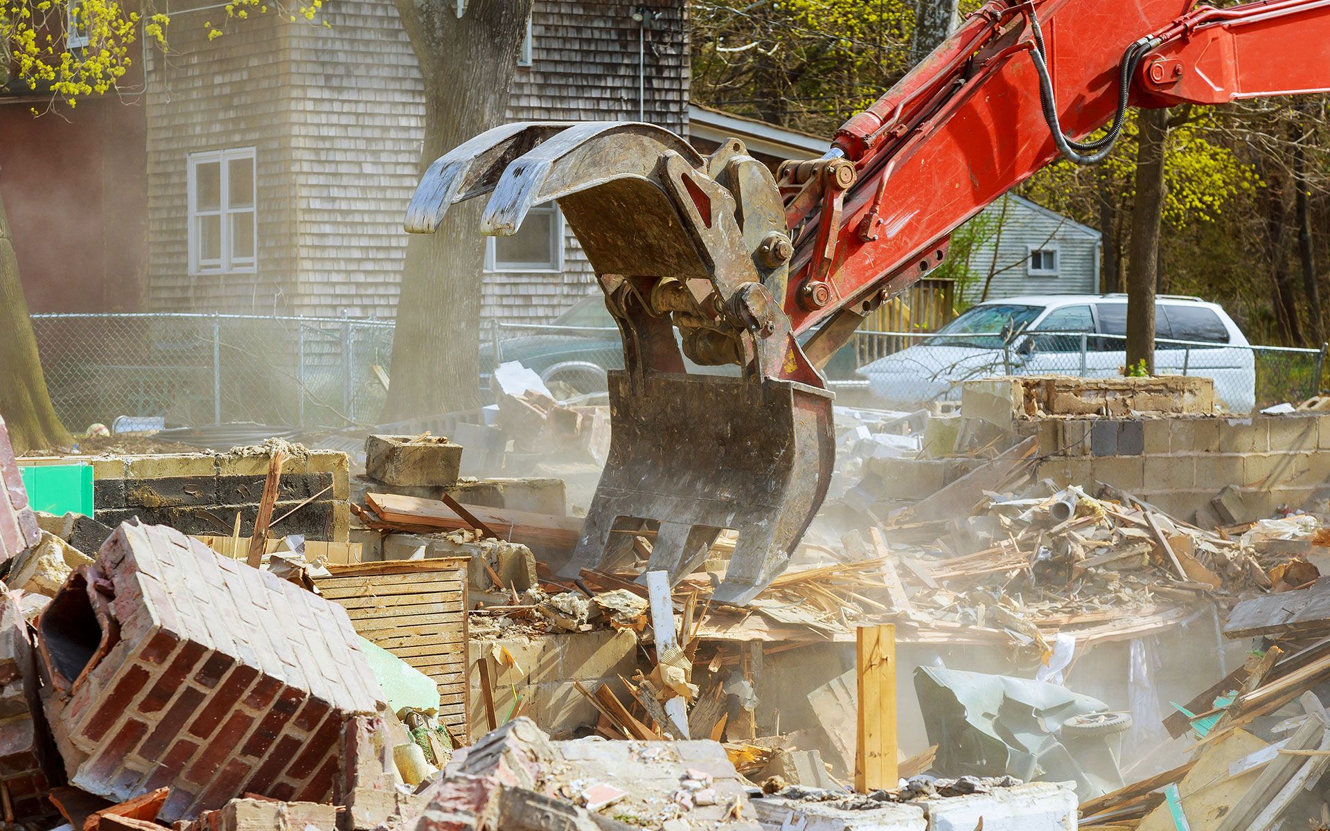 A red excavator is demolishing a brick house.