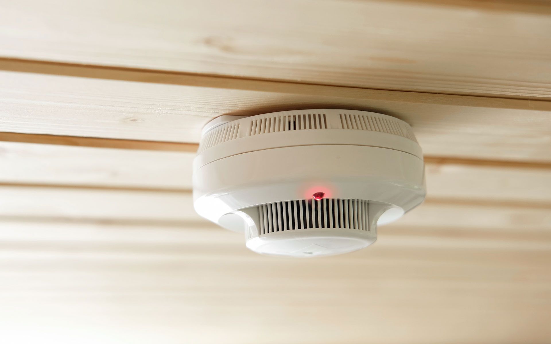 A smoke detector is hanging from the ceiling of a wooden room.