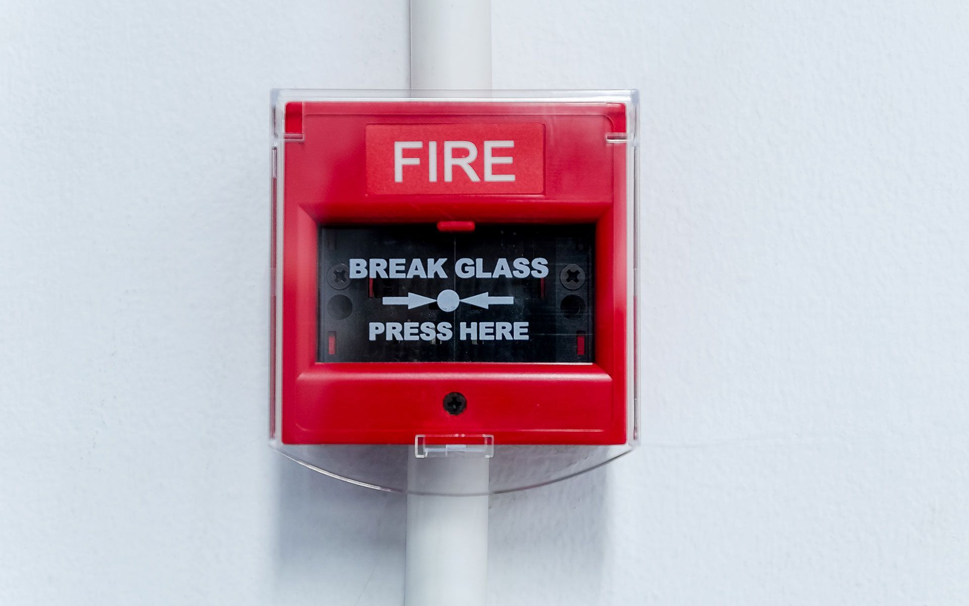 A red fire alarm is hanging on a white wall.
