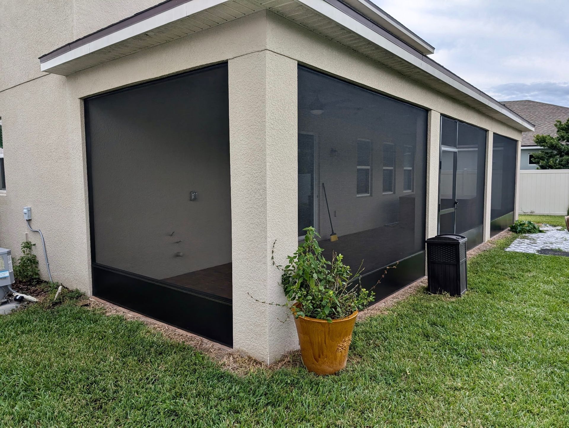 Screened patio with black screens, tan stucco, and a potted plant on green grass.
