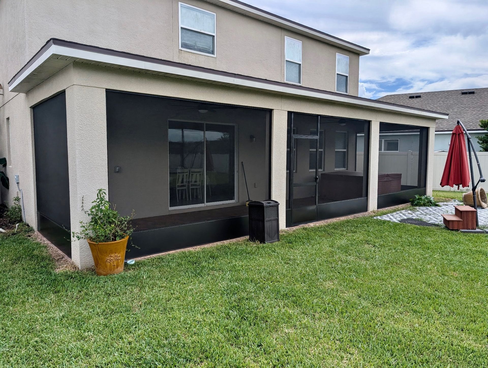 Enclosed patio with black screens, sliding glass door, and potted plant. Back yard with green grass.
