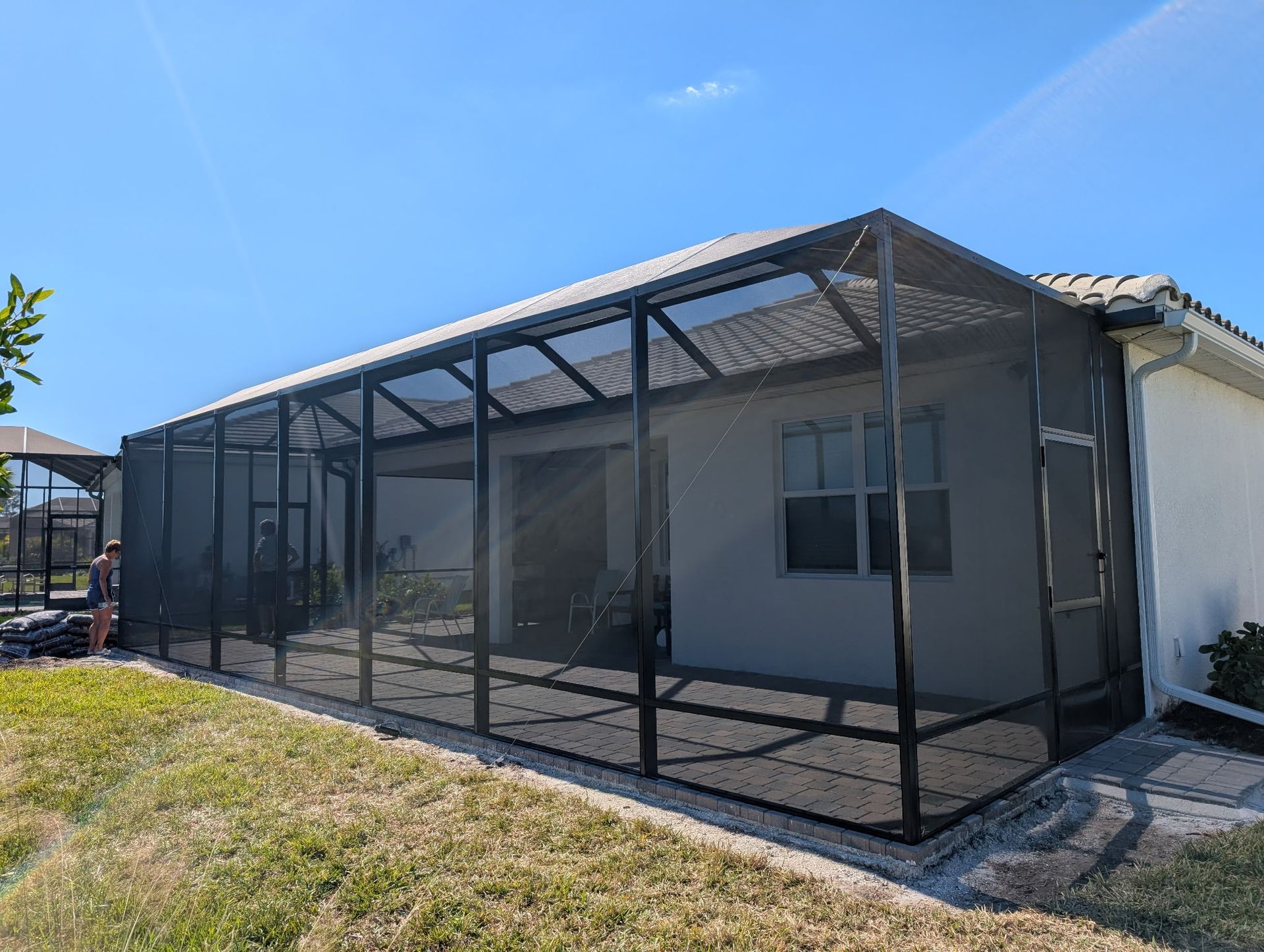 A screened-in patio extension attached to a house with a gray roof, black screens, and a blue sky.