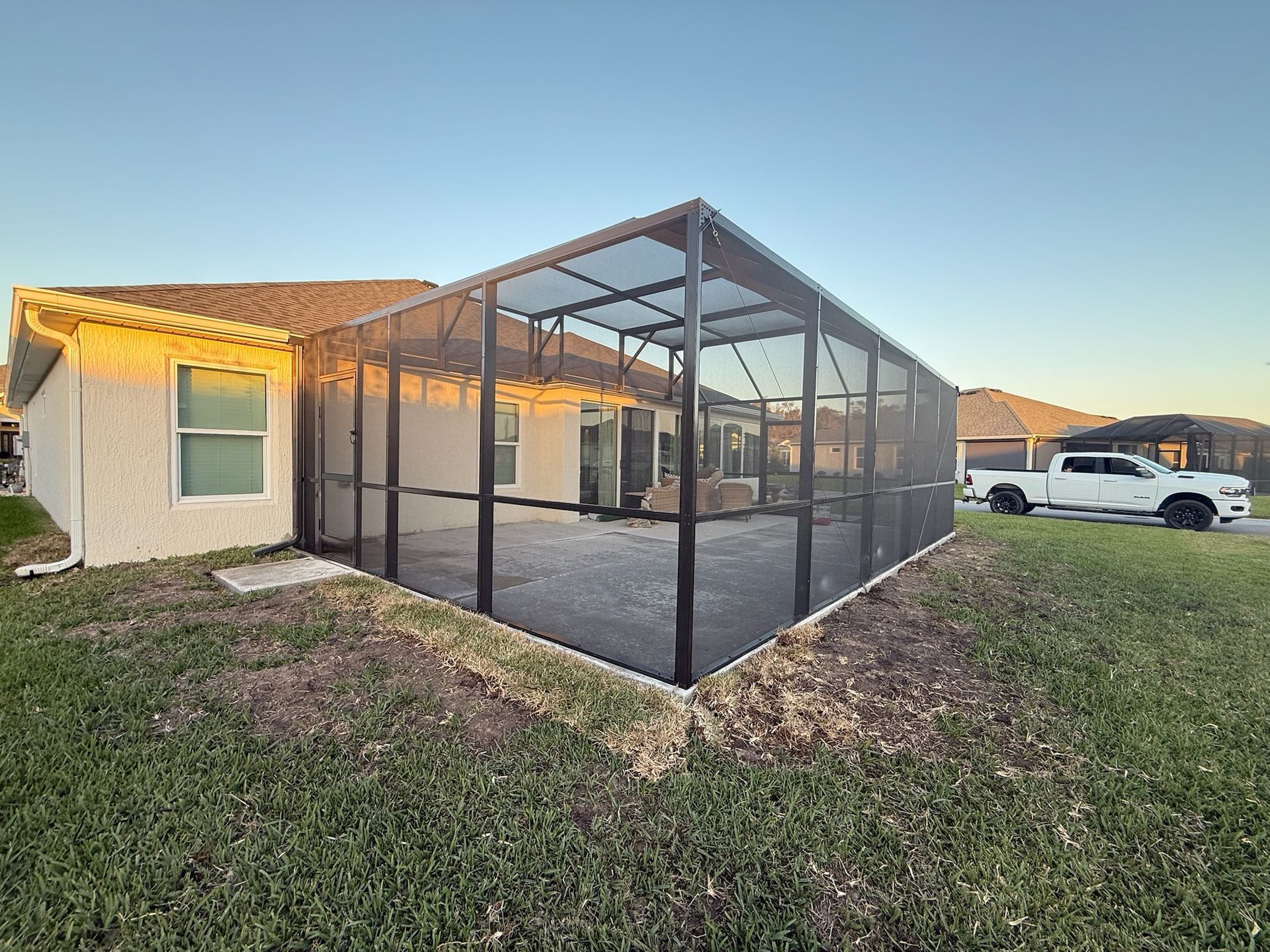 Screened-in patio enclosure attached to a house with a gray concrete floor, and green grass.