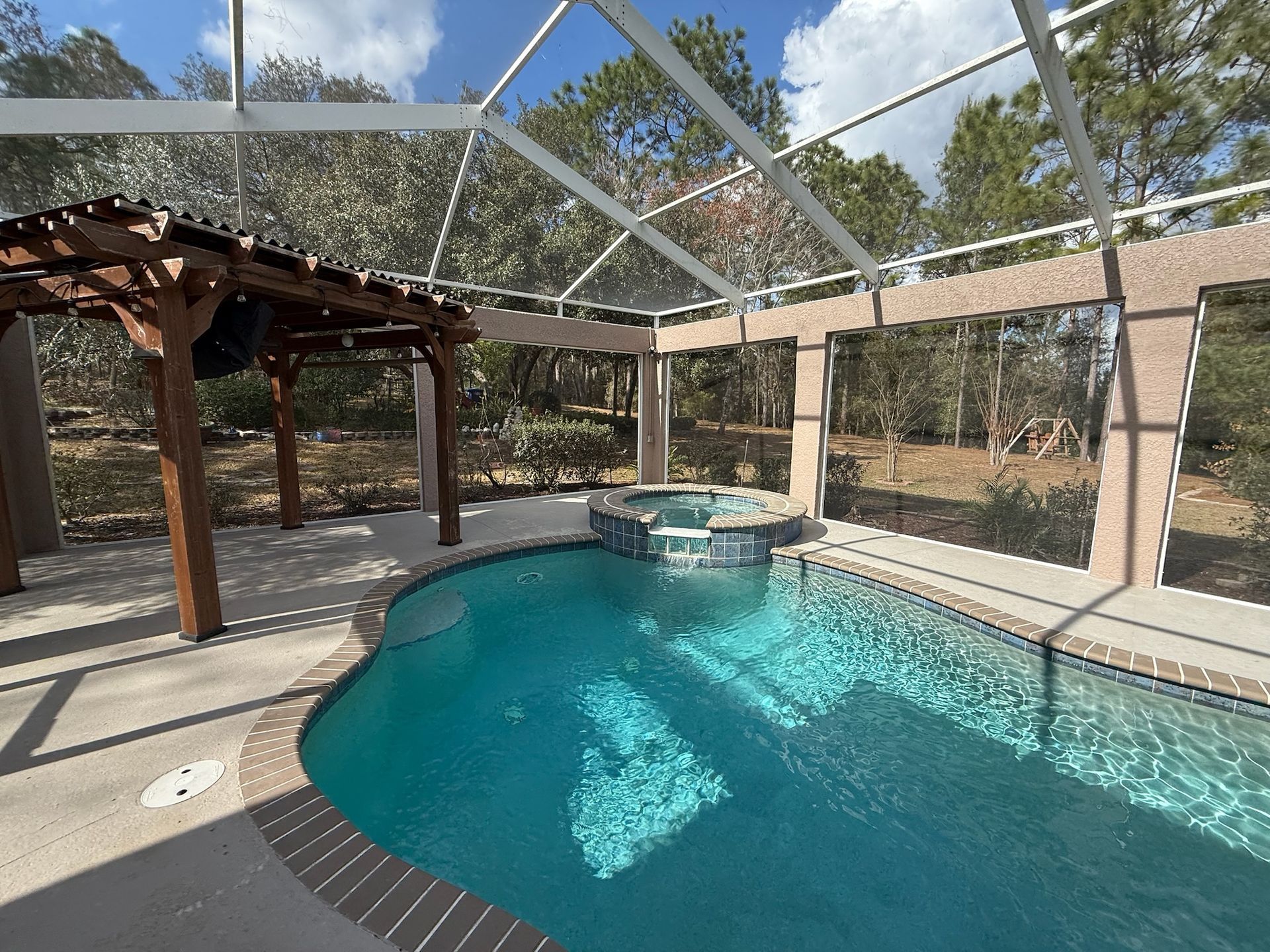 Swimming pool with spa under a screened enclosure and a wooden pergola.