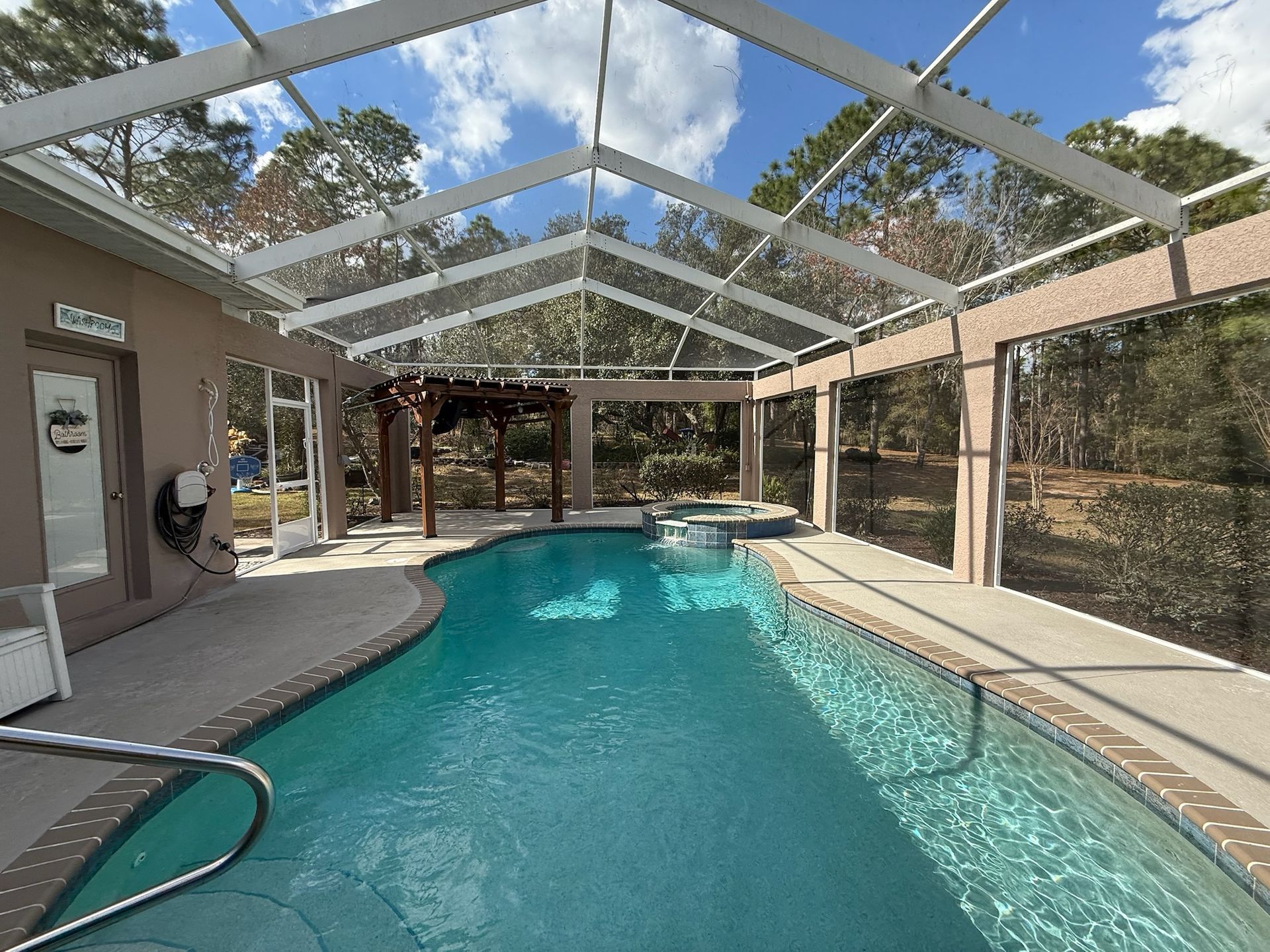 Pool enclosed in a screened patio, overlooking a wooded area. The pool is filled with clear blue water.