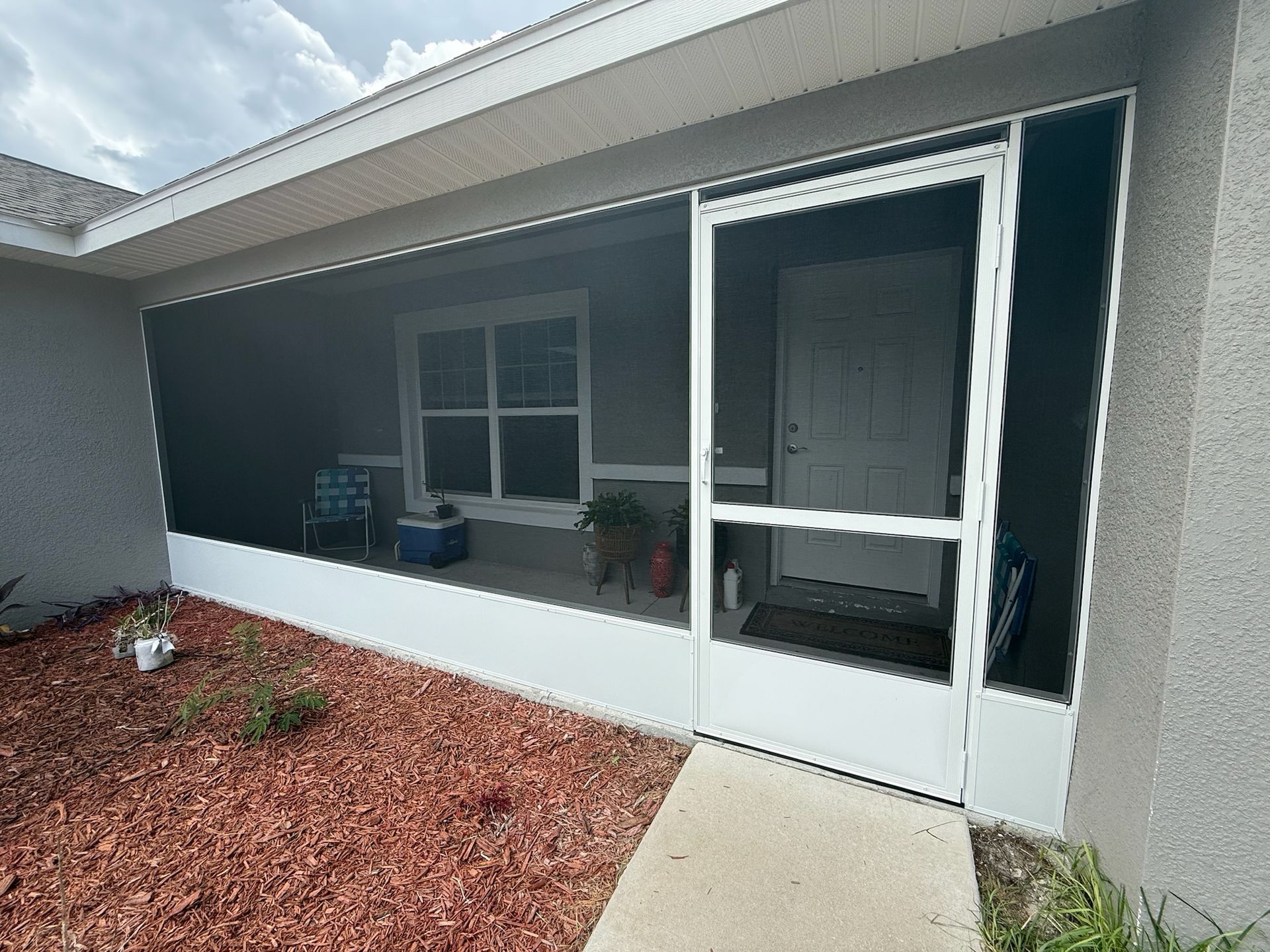 Screened porch with white frame, grey siding, and red mulch.