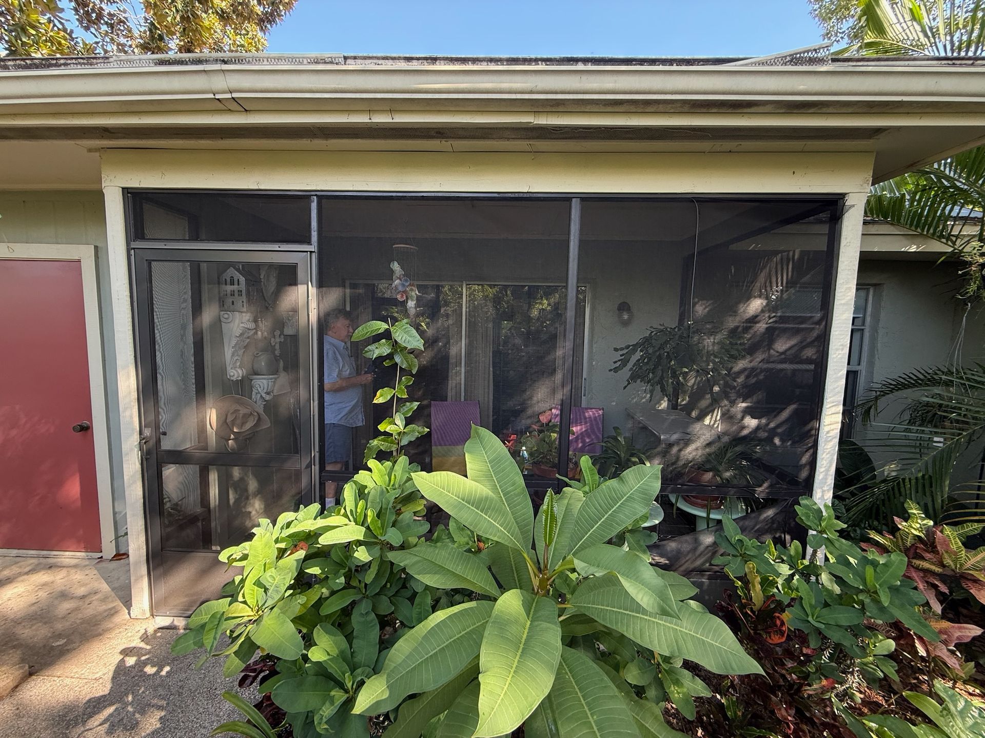 Screened-in porch with a person visible inside; lush green plants in front.