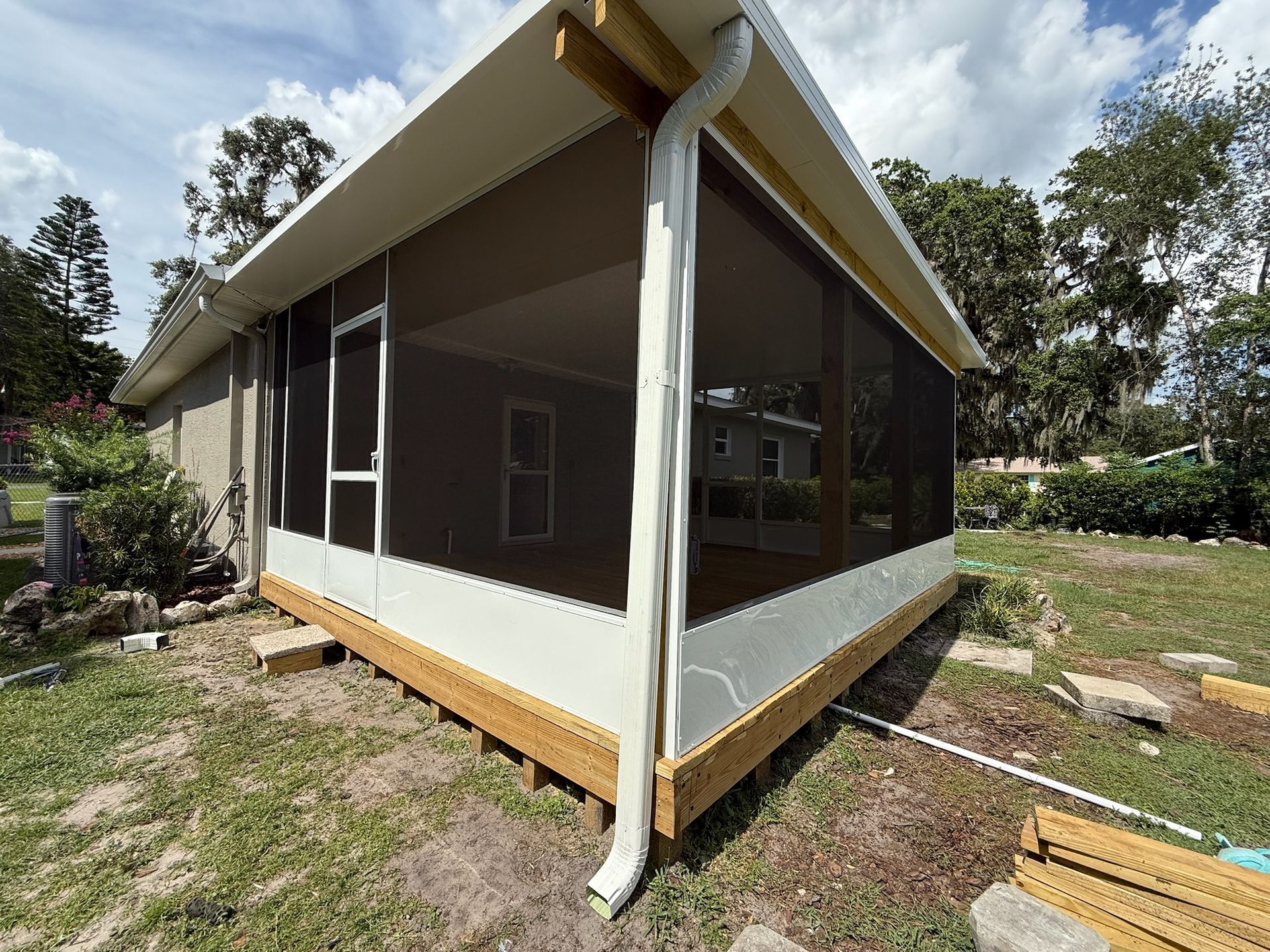 Screened porch with white trim, brown screens, and wooden deck in a grassy backyard.