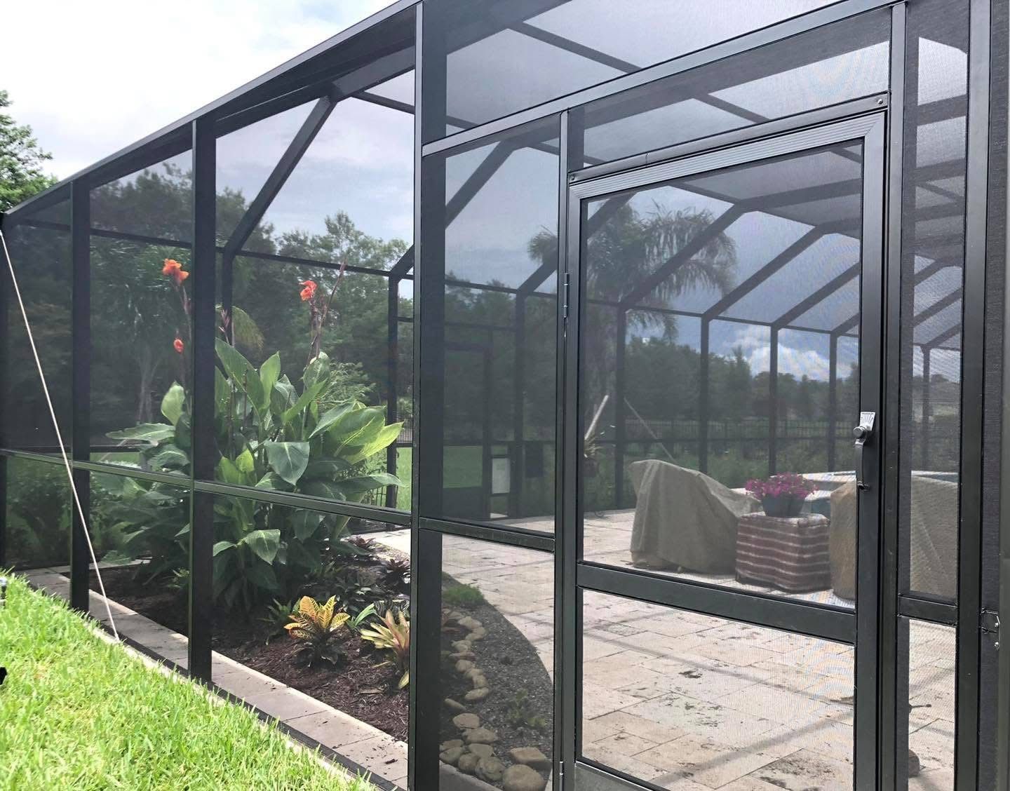 A screened in porch with a patio in the background.