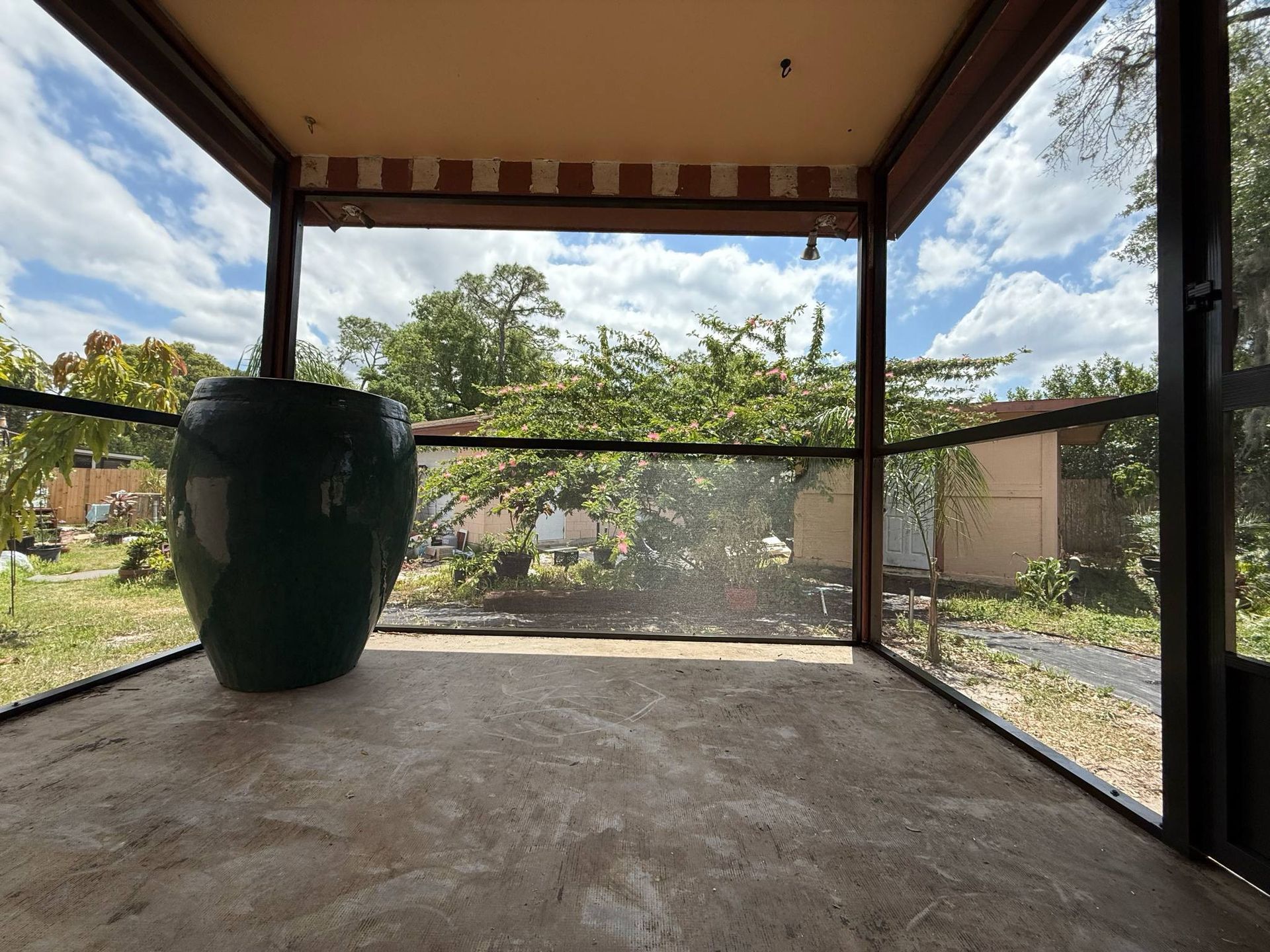 A screened in porch with a large green vase on the floor