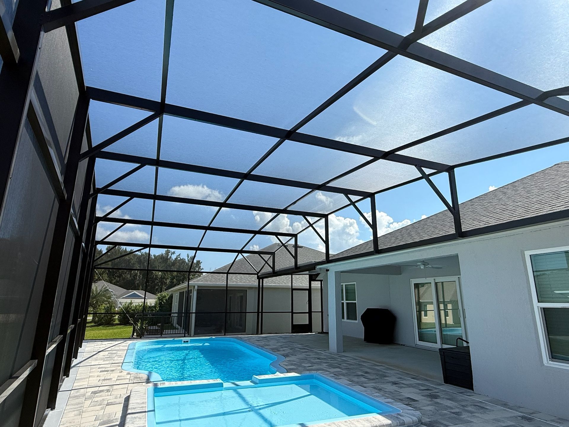 Pool area with screened enclosure under a partly cloudy sky. Pool and patio visible.