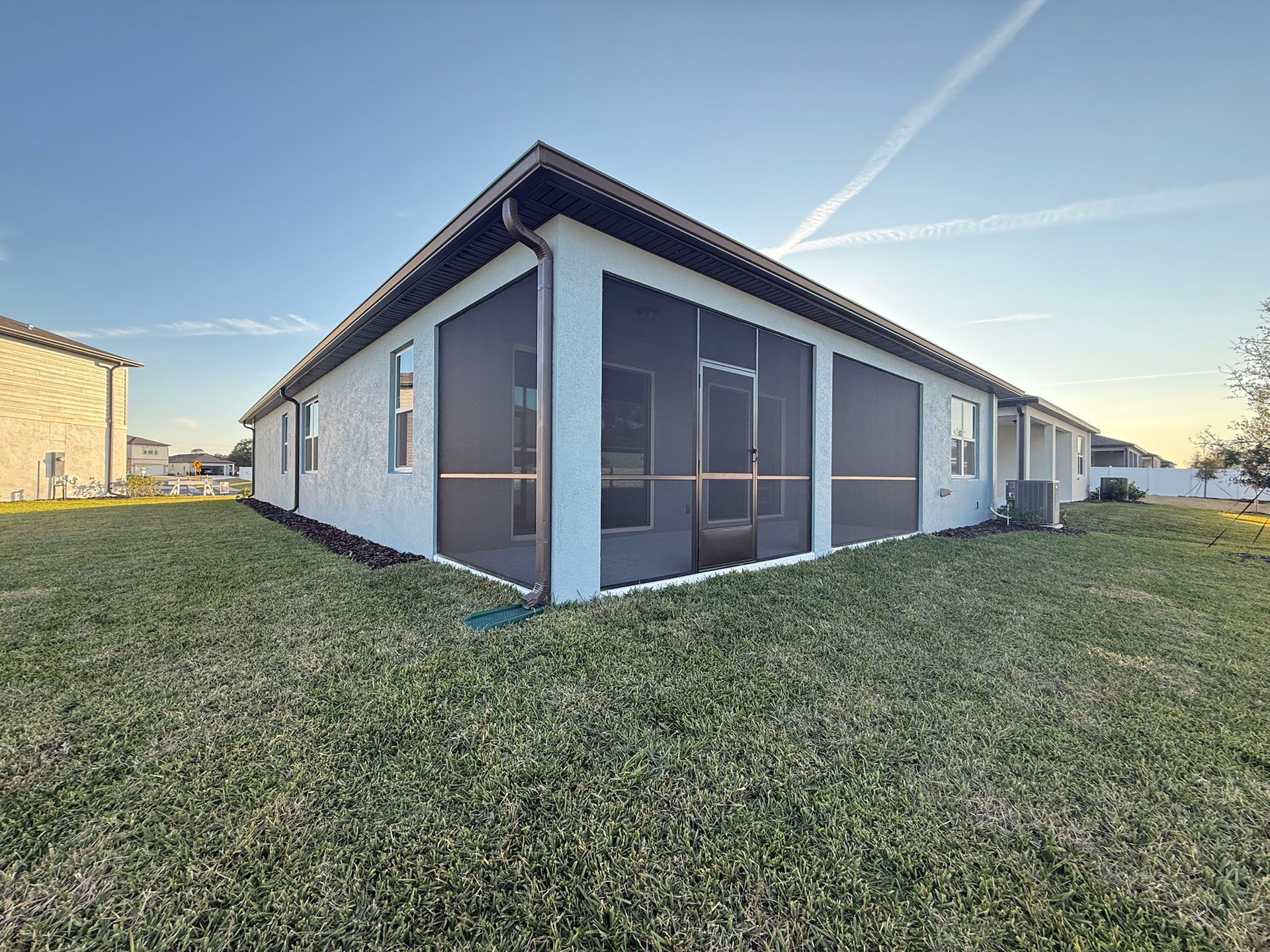 Back of a house with screened-in porch and grassy yard under a blue sky.