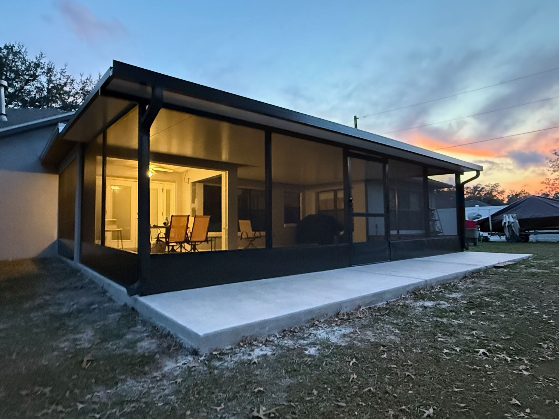 Screened-in patio with concrete slab and dark frame, attached to a house, at dusk.