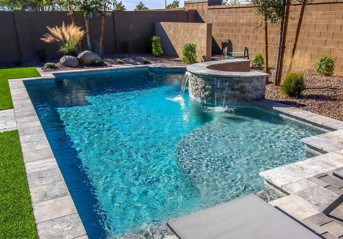 A large swimming pool with a waterfall in the backyard of a house.