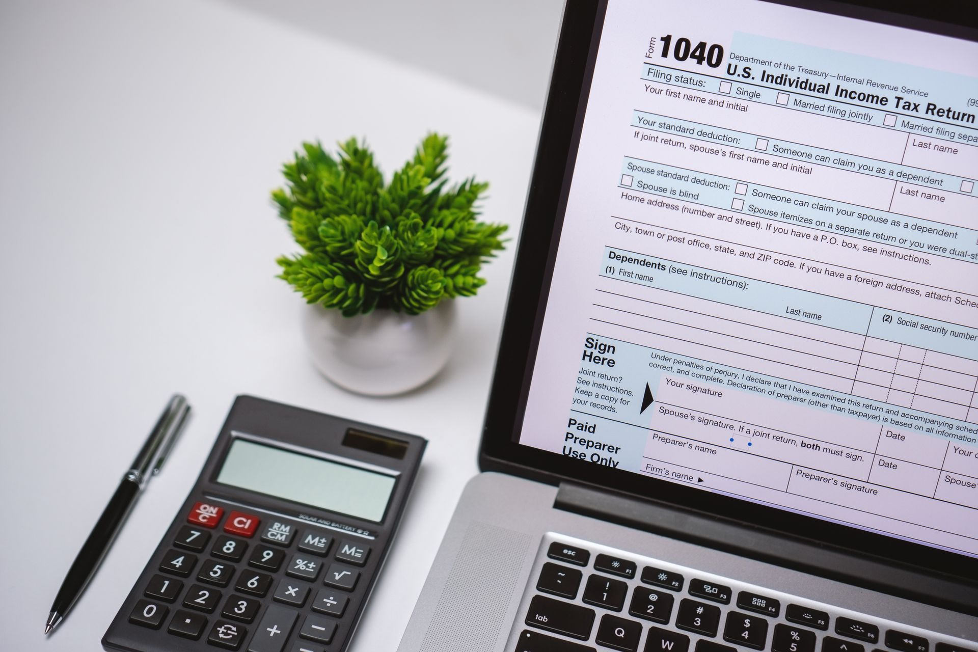 High angle view of tax form on laptop screen on work desk with pen, calculator and a small plant.