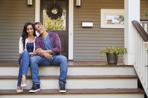A young couple sits on the porch of their single family home and smiles at the camera