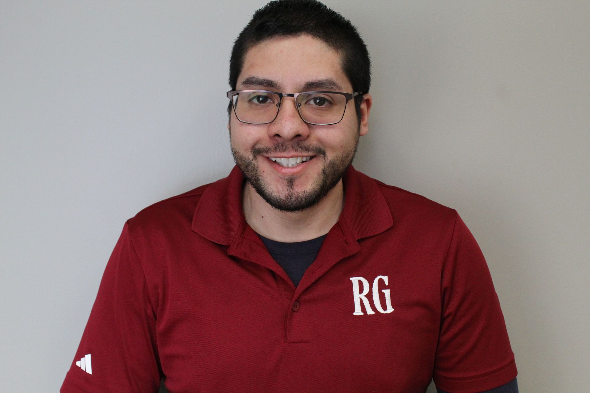 A Man Wearing Glasses and A Red Shirt with The Letter Rg on It.