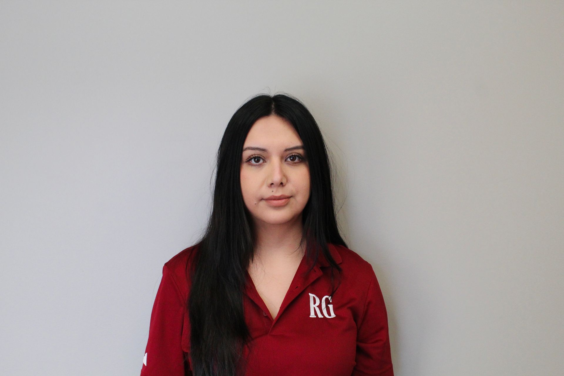 A Woman in A Red Shirt Is Standing in Front of A White Wall.