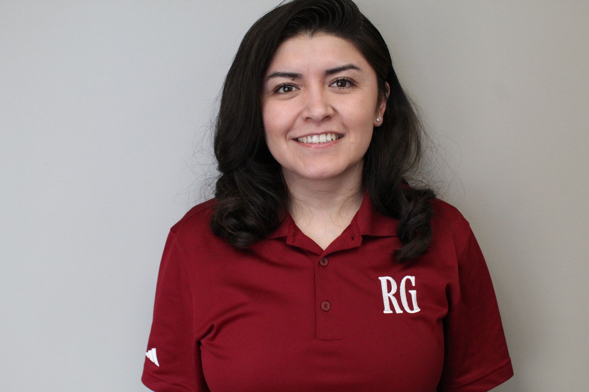 A Woman Wearing a Red Polo Shirt with The Letter Rg on It Is Smiling.