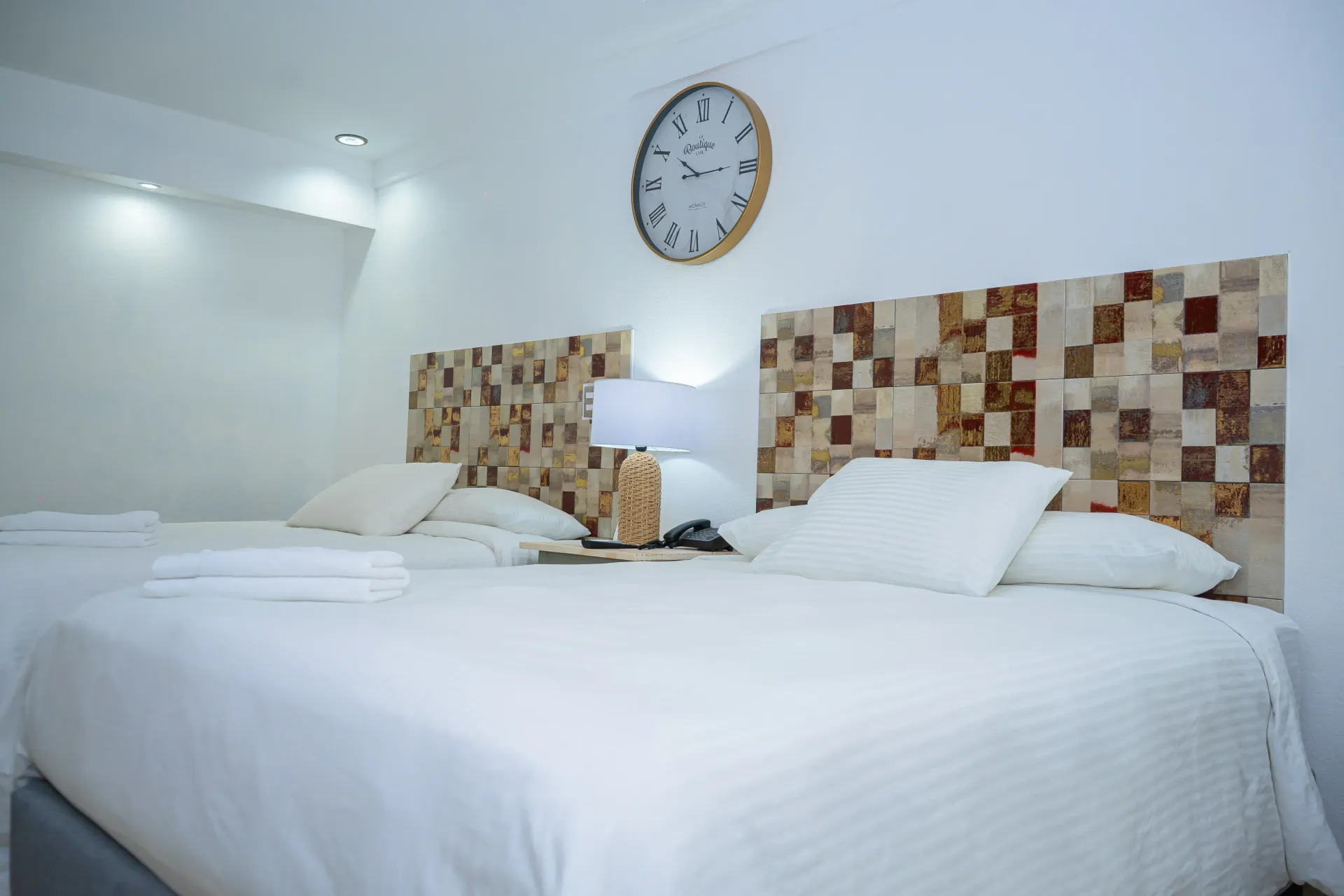 Dos camas con cabeceros decorativos en una habitación luminosa, con un reloj en la pared.