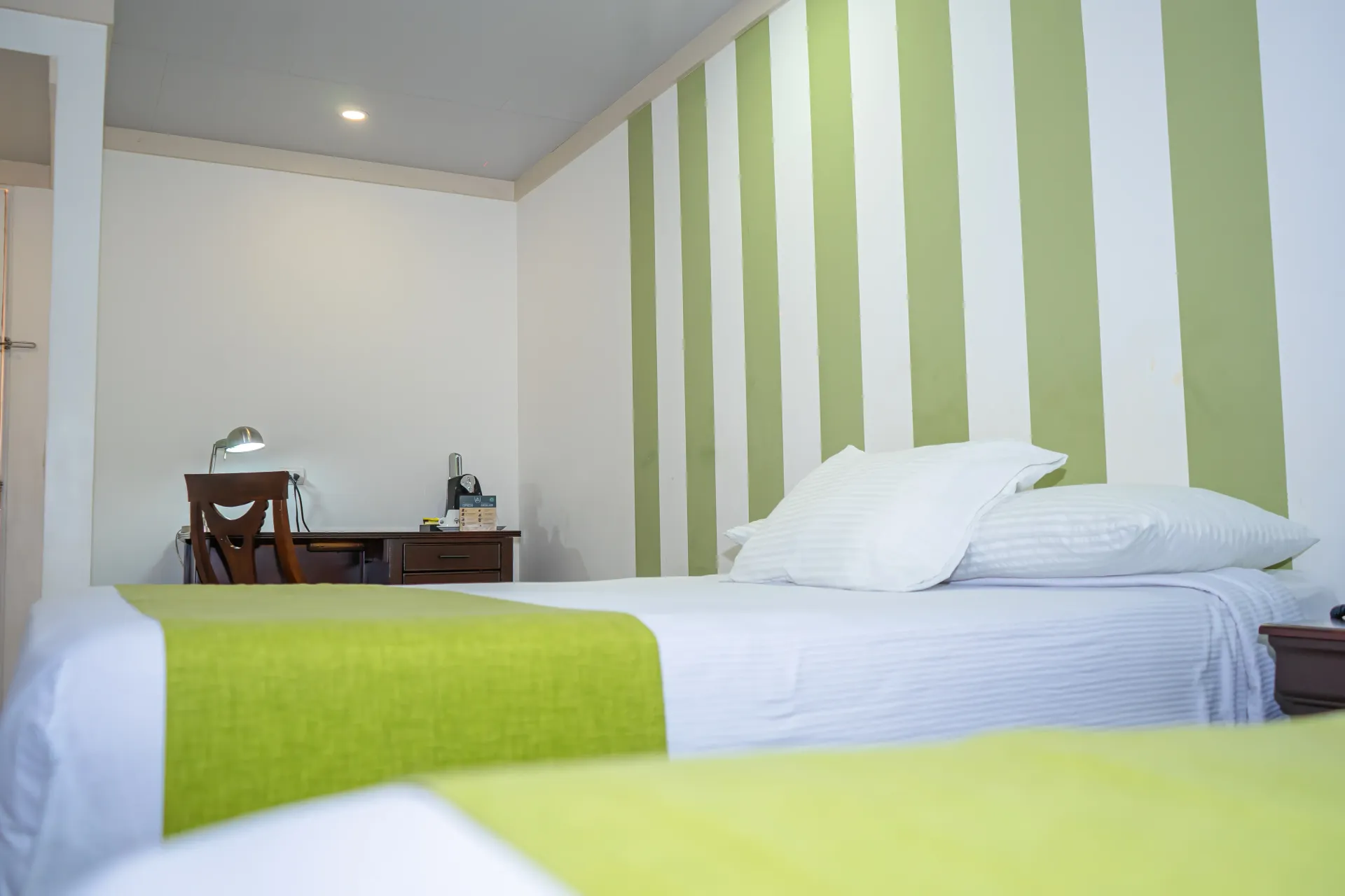 Dormitorio con dos camas, pared con acento de rayas verdes y un escritorio.