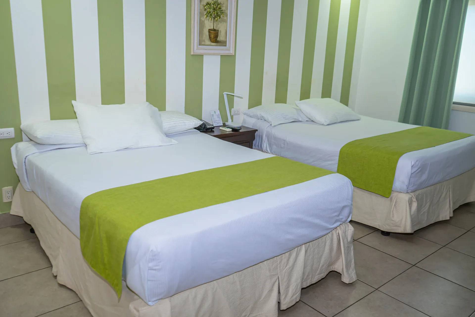 Dos camas con sábanas blancas, caminos de cama verdes, en una habitación con papel pintado de rayas verdes y blancas.