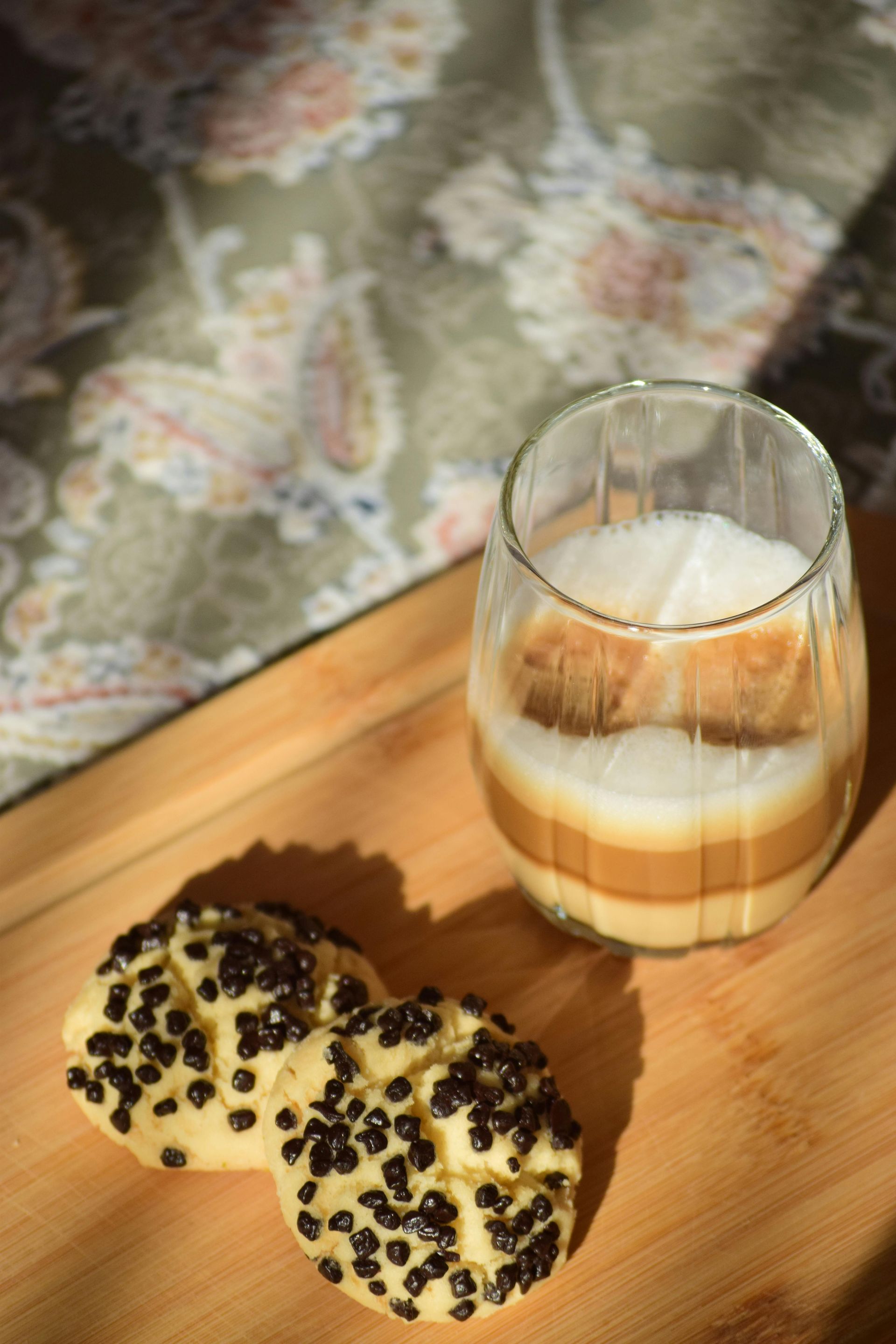 Vaso de bebida en capas y dos galletas con chispas de chocolate sobre una tabla de madera.