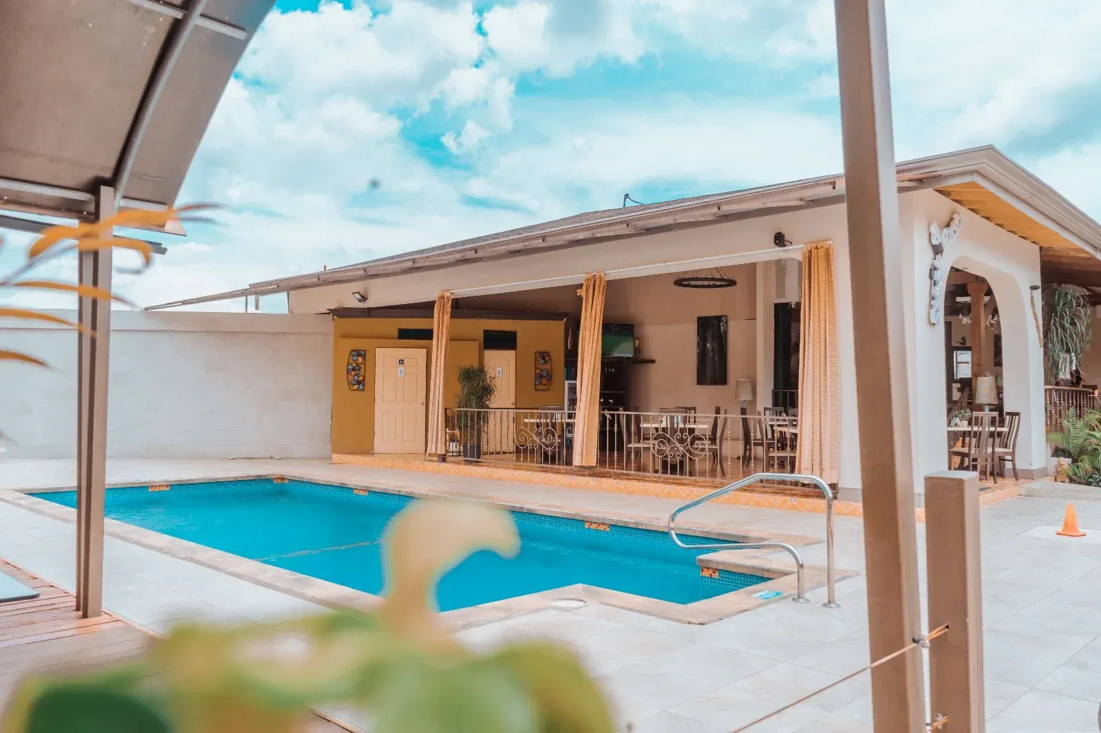 Área de comedor al aire libre junto a la piscina con piscina azul, cielo nublado y restaurante.